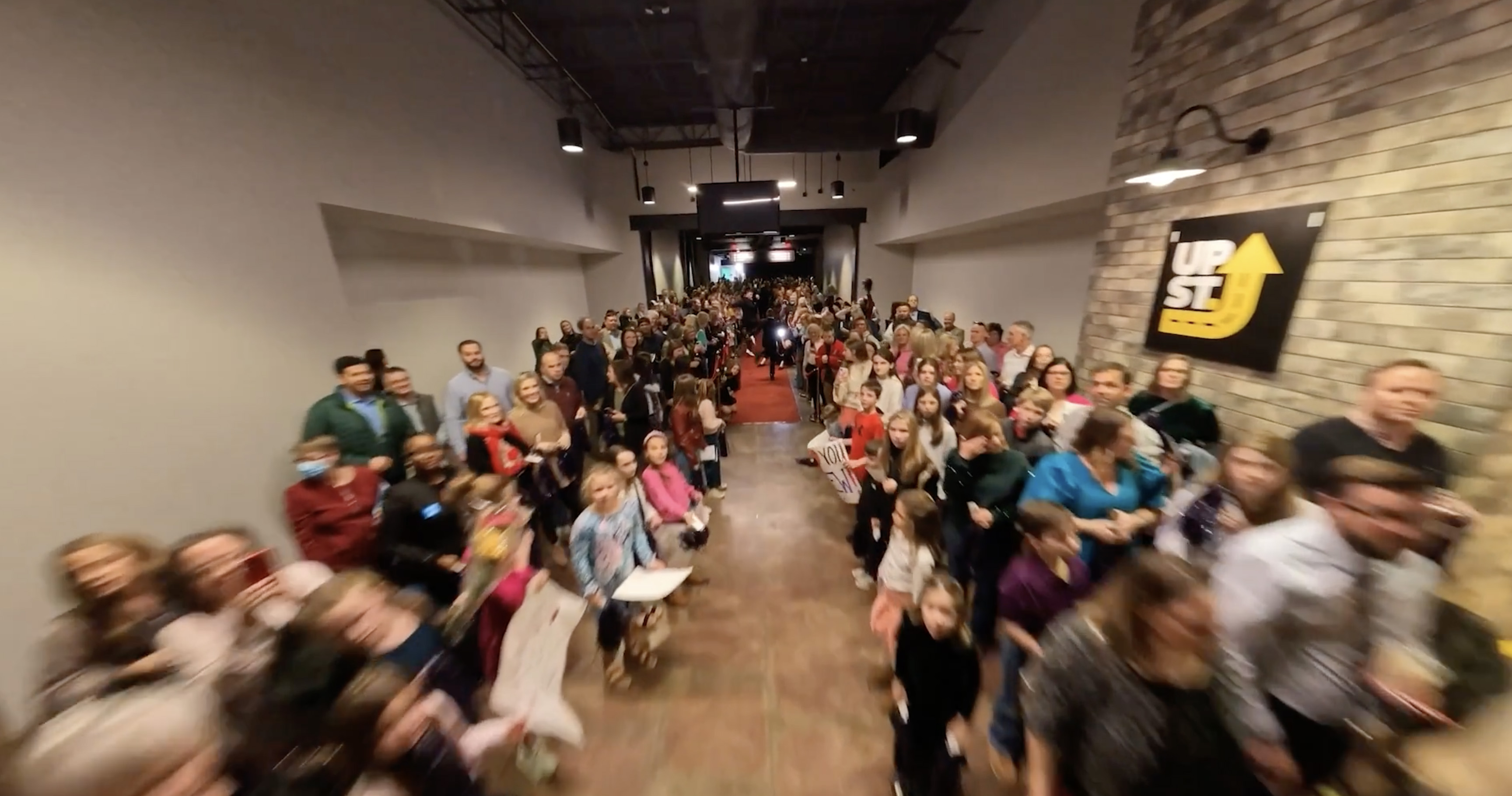 FPV drone flying through crowded event with red carpet